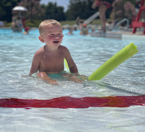 Little boy playing with a pool noodle in the shallow end of a swimming pool